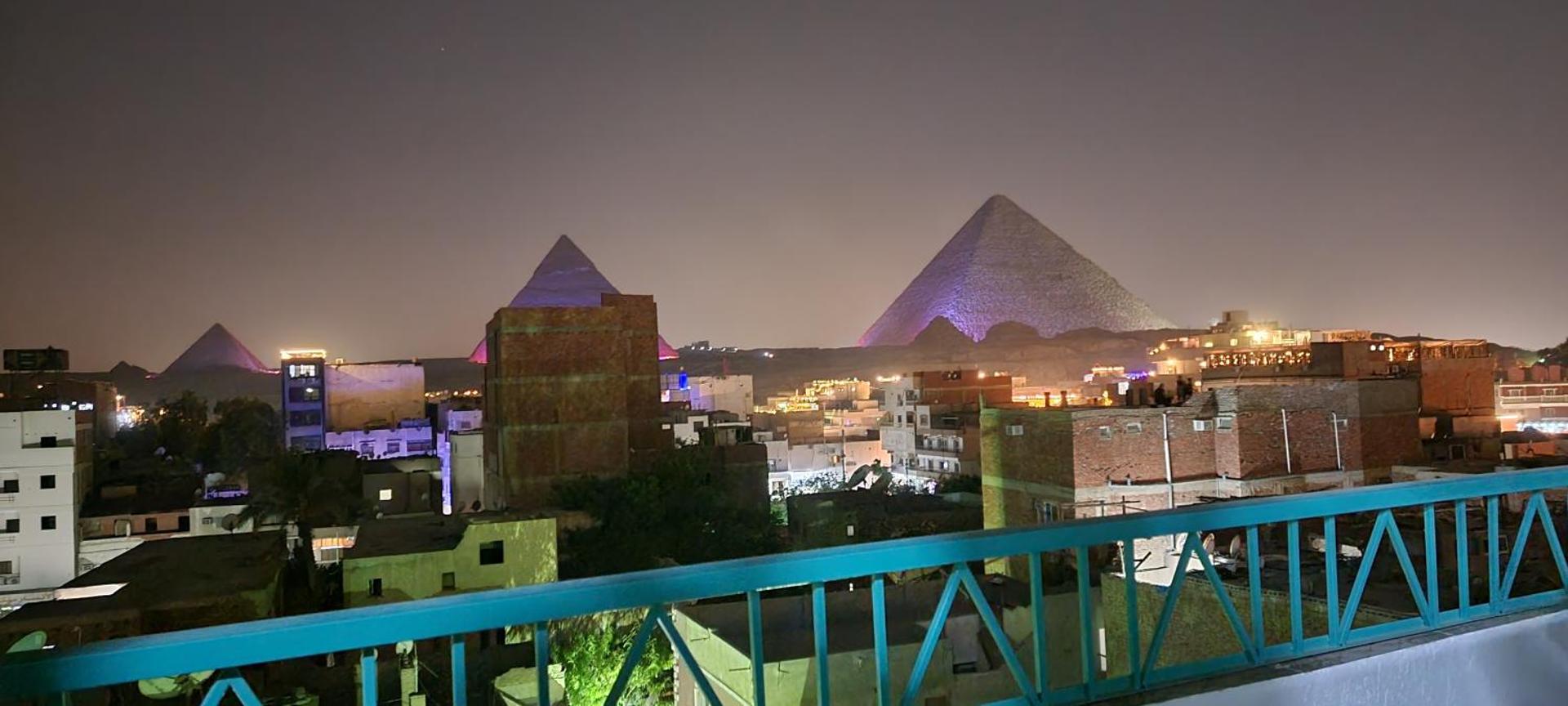 The pyramids lit up at night above the rooftops of Nazlet El-Semman