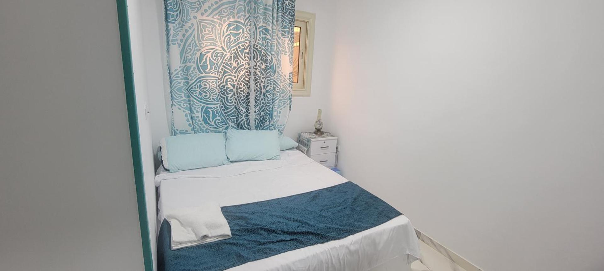 Double room with a large bed, blue linen and a patterned curtain
